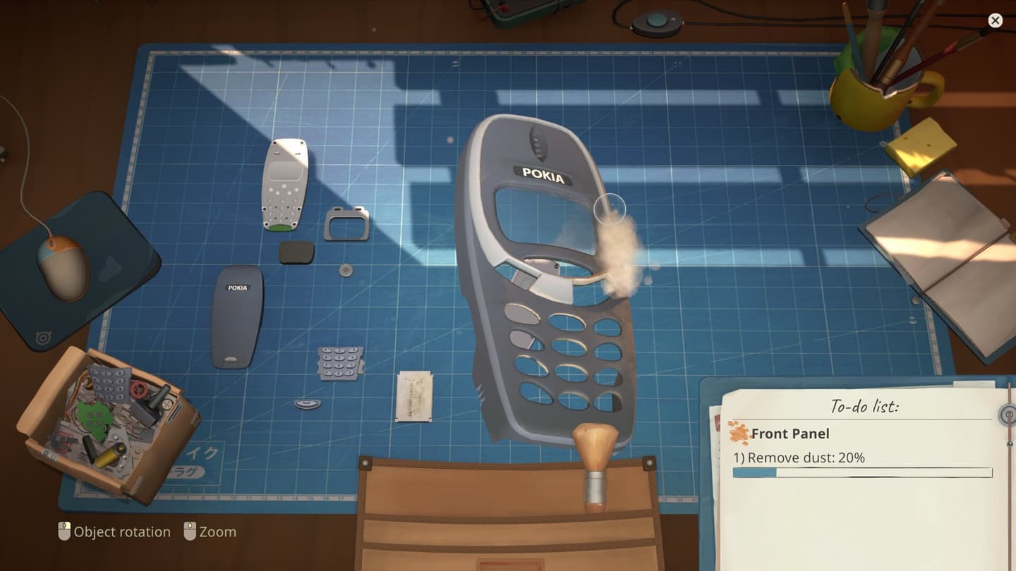 A grey handheld-style front shell sits on a blue cutting mat with a separate back cover, keypad, and small components.